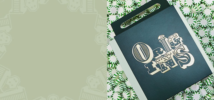 sage green background with emerald green Origins gift box on top of green peppermint candy